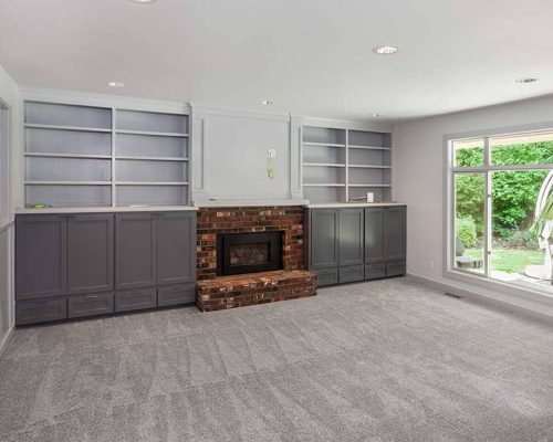 Sea Breeze A spacious living room with gray carpet, built-in shelves, a brick fireplace, and a large window overlooking a green outdoor area. Enjoy the refreshing sea breeze as it flows through the clean windows. Floor And Window Cleaning