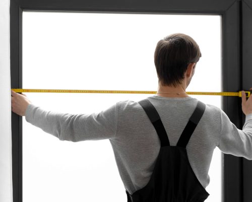 Sea Breeze A person in overalls measures the width of a window using a yellow tape measure, possibly preparing for some window cleaning. The background is bright white. Floor And Window Cleaning