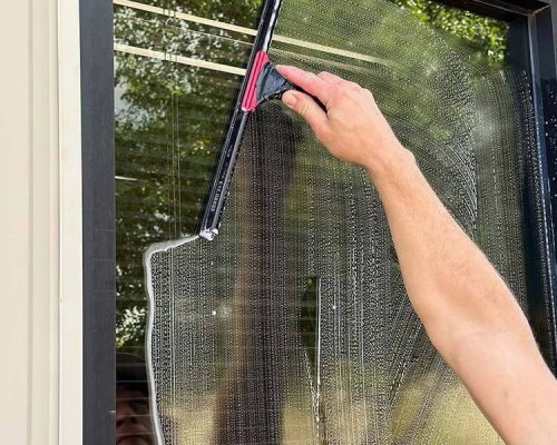Sea Breeze A person's hand is using a black and pink squeegee to clean soapy water from a window, with a clear section in progress. The fresh sea breeze mingles with the scent of cleaning solution, adding an invigorating touch to the task. Floor And Window Cleaning